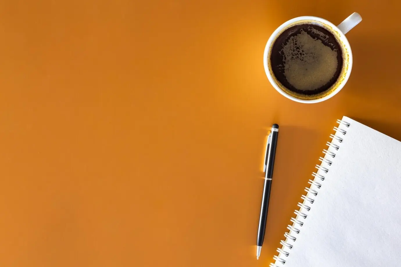 Notizblock, Stift und Tasse Kaffee auf braunem Hintergrund in Draufsicht