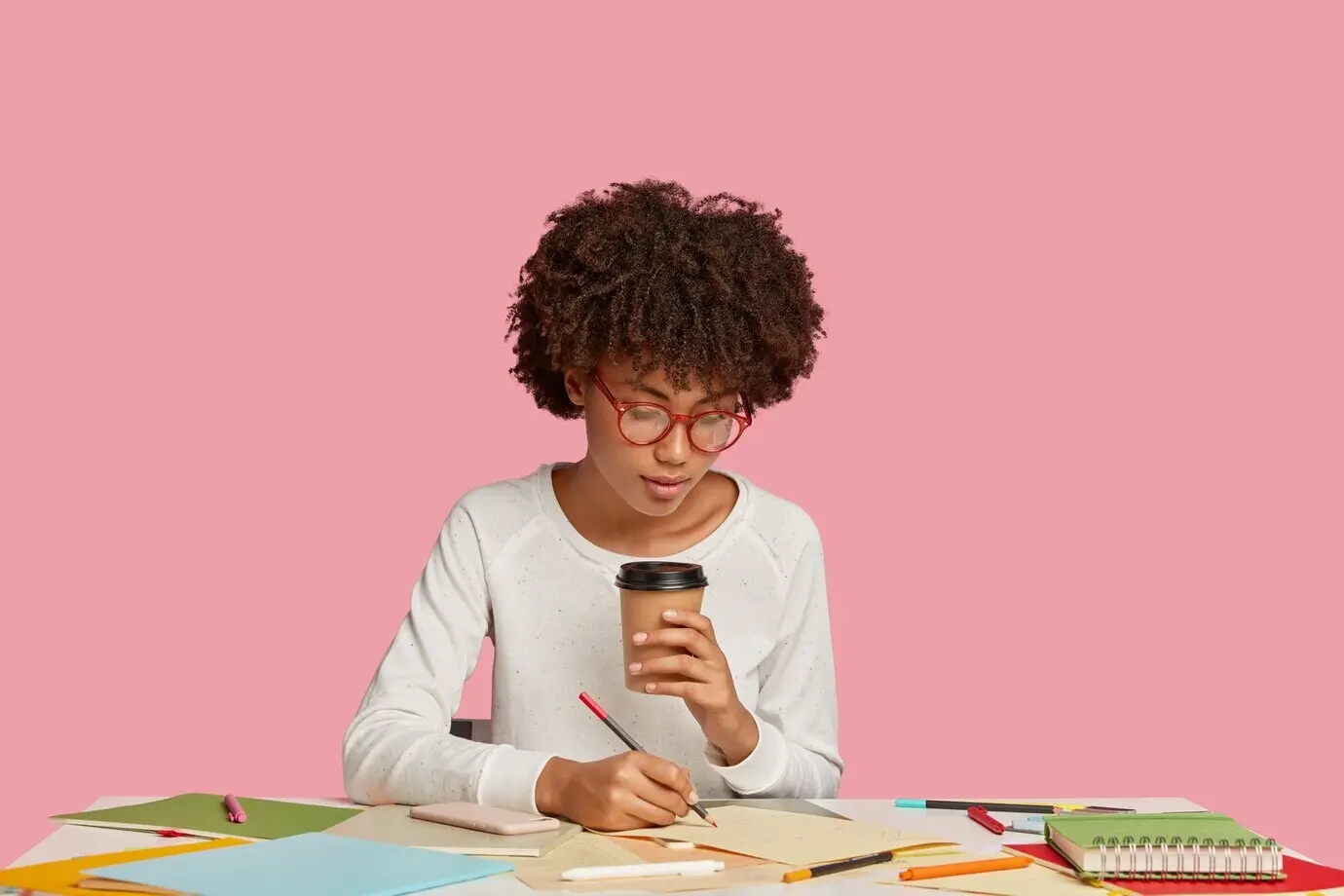 Eine hübsche Studentin posiert am Schreibtisch vor einer rosafarbenen Wand.