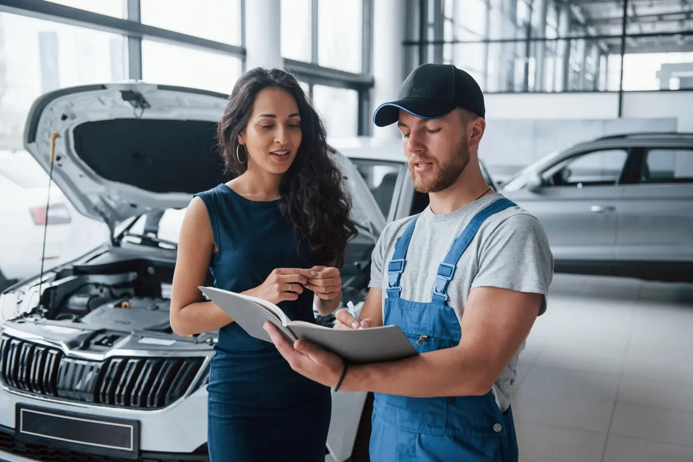 Mit dem Stift schreiben. Eine Frau im Autosalon mit einem Mitarbeiter in blauer Uniform, die ihr repariertes Auto wieder entgegennimmt.